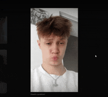 a young man wearing a white shirt and a necklace is making a silly face