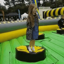 a little girl is standing on a green and yellow inflatable circle with a sign that says event catering in the background