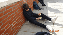 a boy leaning against a brick wall with the date 05 22 2024 on the bottom