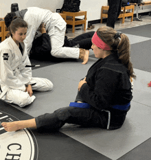 a woman in a karate uniform with the word jiu-jitsu on her sleeve sits on a mat