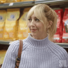 a woman in a purple sweater is standing in front of a dog food shelf in a grocery store .