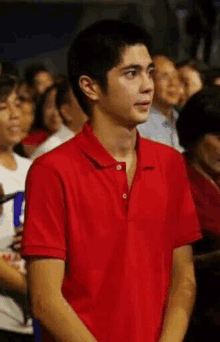 a young man in a red polo shirt is standing in front of a crowd .