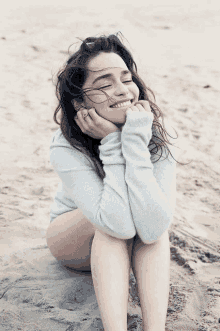 a woman sitting on the beach with her eyes closed