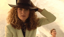 a woman with curly hair wearing a hat and a white suit