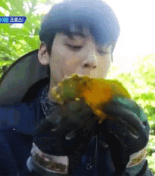 a young man is eating a piece of food with a blue sign in the background that says ' korean ' on it