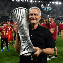 a man in a black shirt is holding a trophy on a soccer field