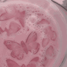 a close up of a bowl of pink liquid with butterflies in it