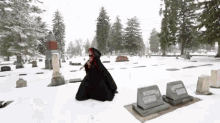 a woman in a black cape stands in a snowy cemetery next to a grave with the name williams on it