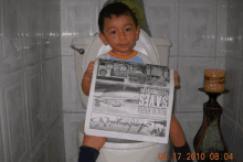 a young boy is sitting on a toilet holding a newspaper that says passenger life