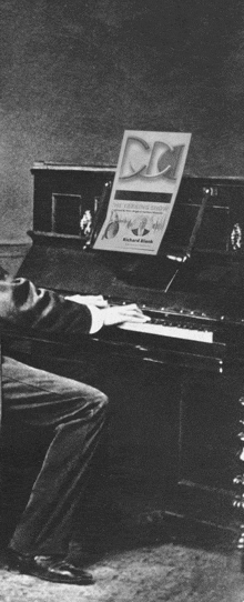 a black and white photo of a man playing a piano with a cd on top