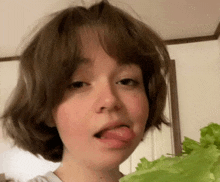 a girl with short hair is sticking her tongue out while holding a piece of lettuce .