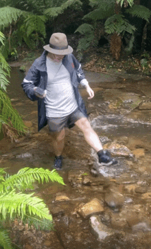 a man wearing a hat is crossing a stream in the woods