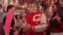 a group of people are dancing in a room with a man wearing a mask and a letter c jacket .