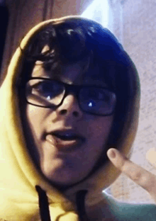 a person wearing a yellow hoodie and glasses is making a funny face .