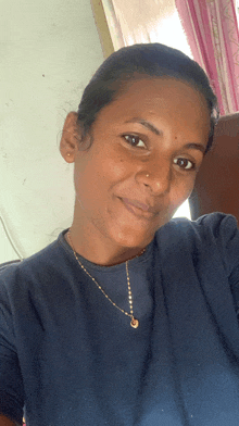 a woman wearing a blue shirt and gold necklace smiles for the camera