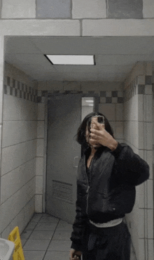 a person taking a selfie in a bathroom with a yellow caution sign on the floor