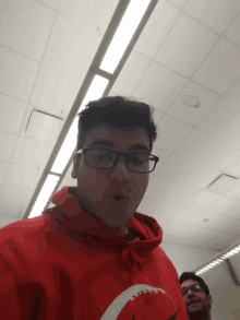 a young man wearing glasses and a red hoodie stands in a room