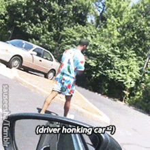 a man in a hawaiian shirt is walking down a road while a car is parked on the side of it