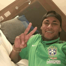 a man wearing a green shirt that says brasil guarana antarctica giving a peace sign