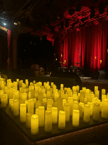 a bunch of yellow candles on a table in front of a red curtain