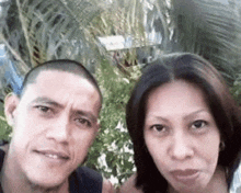 a man and a woman are posing for a selfie in front of palm trees .