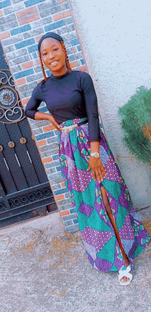 a woman wearing a black top and a purple skirt is standing in front of a brick wall