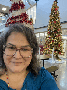 a woman wearing glasses is standing in front of two christmas trees