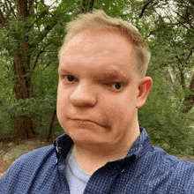 a man in a blue shirt is making a funny face while standing in the woods .