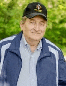 a man wearing a hat and a blue jacket is standing in front of trees .