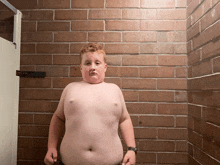 a young boy stands in front of a brick wall without a shirt on