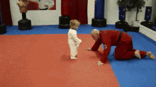 a man in a red karate uniform is kneeling down next to a small child in a white karate uniform .