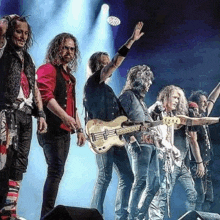 a group of men are standing on a stage holding guitars and singing .