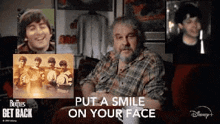 a man with a beard is sitting on a couch in front of a collage of photos of the beatles .