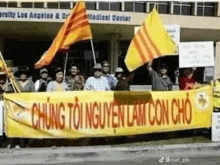 a group of people are standing in front of a building holding flags and a yellow banner .