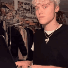 a young man wearing a black sweater and a skull necklace is using a laptop