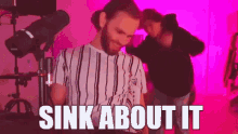 a man with a beard is standing in front of a microphone with the words `` sink about it '' written on the screen .