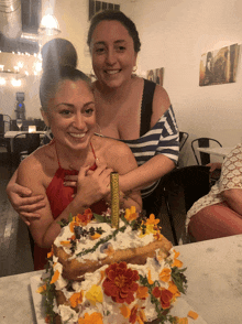 two women standing next to a cake with a candle on it