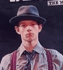 a young man wearing a hat and suspenders is standing in front of a wall .