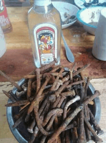 a bowl of rusted nails next to a bottle of rum