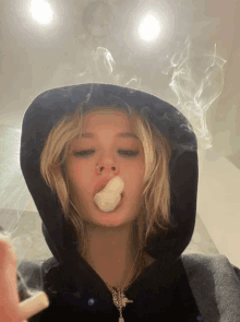 a woman wearing a black hoodie smoking a cigarette