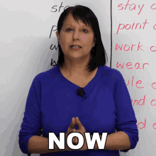 a woman in a blue shirt is standing in front of a white board with the word now on it