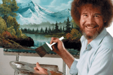 bob ross is smiling while painting a landscape with a brush