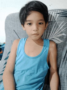 a young boy wearing a blue tank top is sitting on a couch