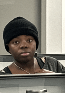 a woman wearing a black beanie and a gray shirt looks at the camera