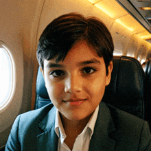 a young boy in a suit sits in a plane