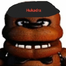 a close up of a teddy bear wearing a black hat with the word hukadra on it .