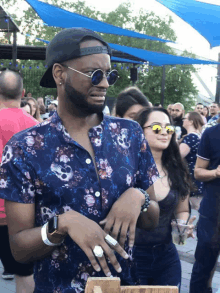 a man wearing a hat and sunglasses stands in a crowd of people