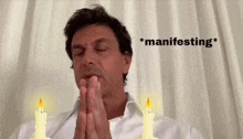 a man praying with two candles in front of him and the word manifesting in the corner