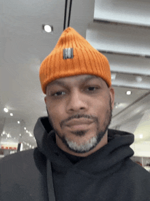 a man wearing a black hoodie and an orange beanie with the letter i on it