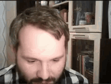 a man with a beard looks at the camera in front of a glass cabinet with a bottle of coca cola on it